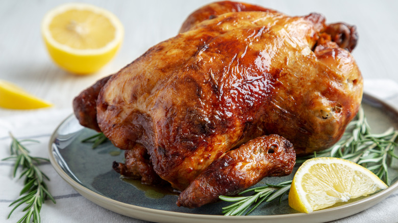 Whole rotisserie chicken on a plate on top of herbs