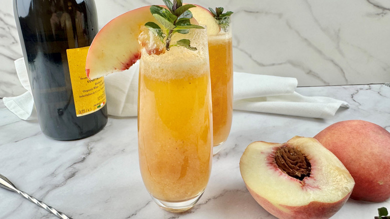 two orange-colored cocktails garnished with peach slices and mint