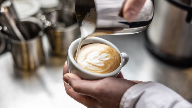 Hand pouring steamed milk into a cup of coffee