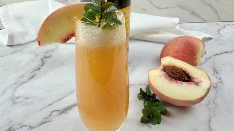 orange-colored cocktail garnished with a peach slice and mint