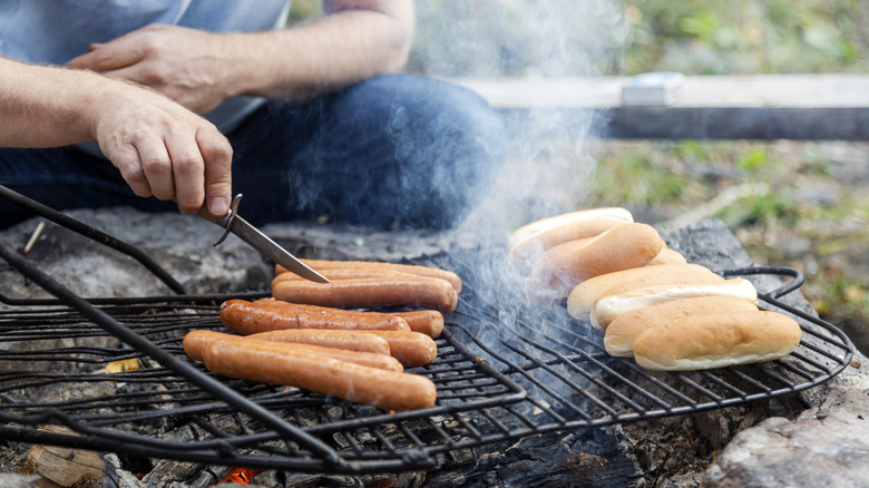 Man grilling hot dogs outside on a wood fire