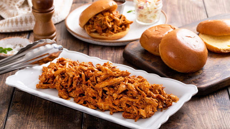 Pulled barbecue chicken on platter next to buns