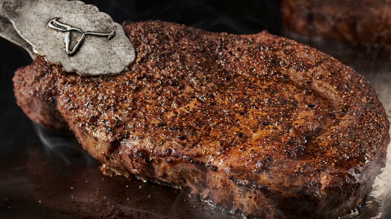 Ribeye steak being grilled at LongHorn Steakhouse with tongs