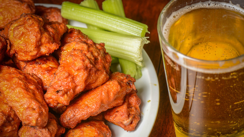 A closeup of a plate of spicy wings, celery, and a beer.