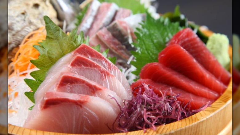 A wooden bowl with sashimi, thinly sliced vegetables and leaves for a garnish